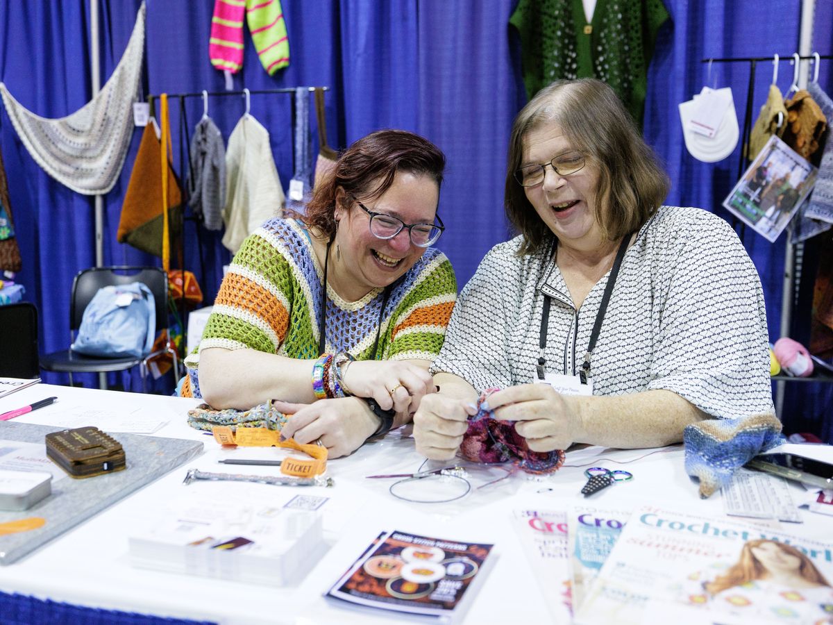 Two festival-goers laughing together over a table of yarn and works in progress